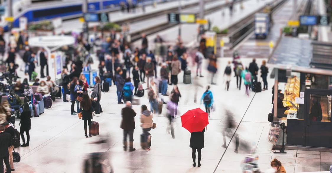 woman with red umbrella waiting at train station and blurred people in motion