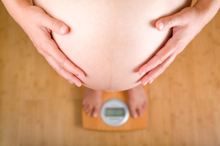 Pregnant woman weighing herself on a bathroom scale. View from above.