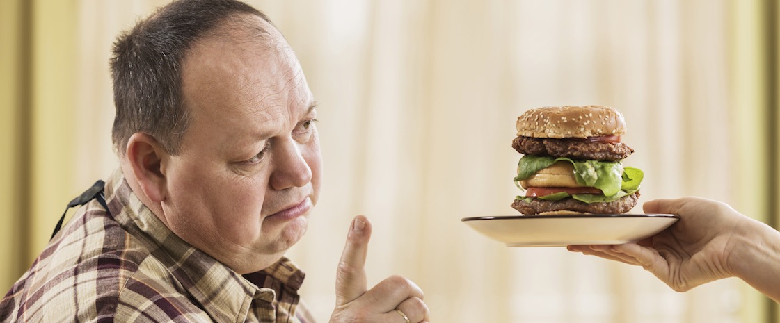 Overweight man refusing a hamburger with a hand sign.