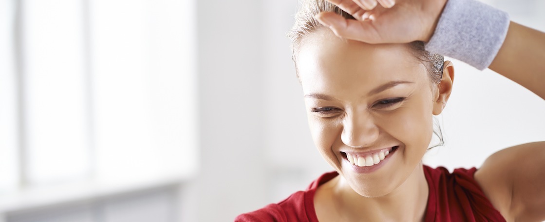 Cheerful woman wiping sweat from forehead after workout