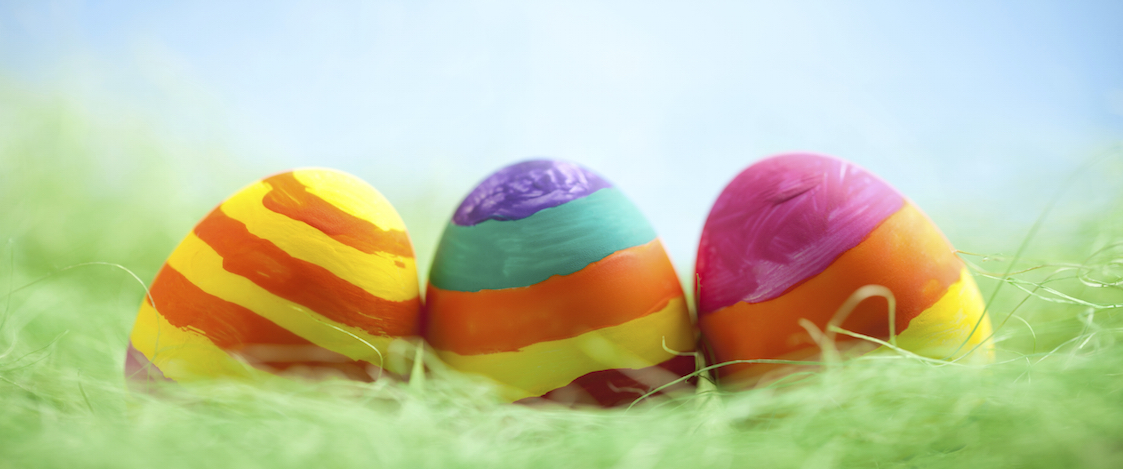 Colorful easter egg with dry green grass on blurred blue background.