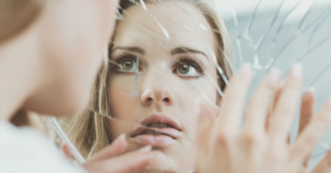 woman looking in cracked mirror