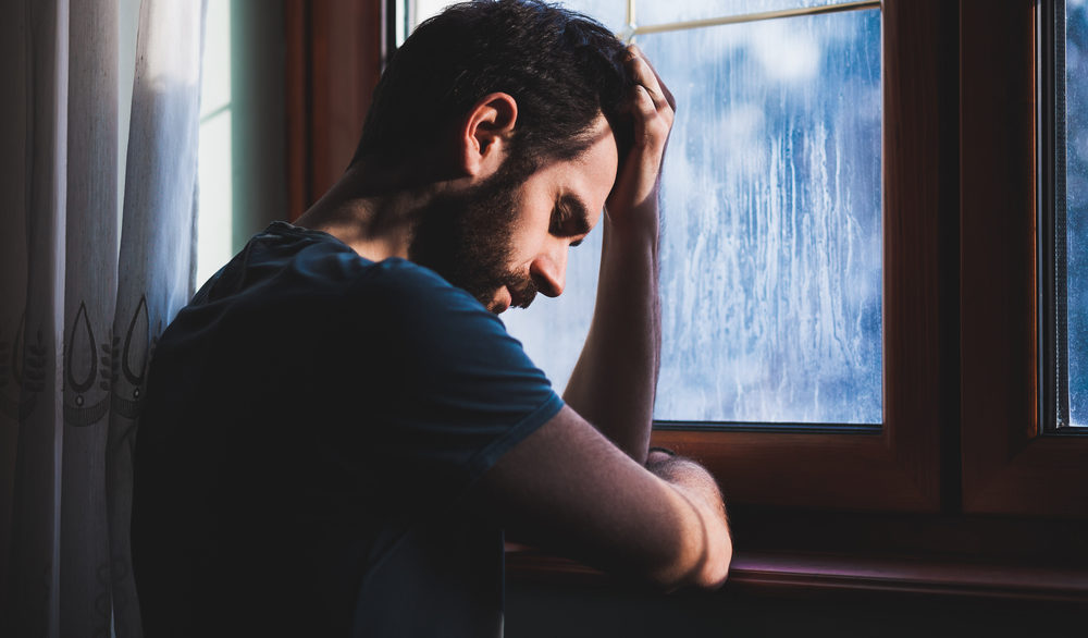 man standing near window depressed